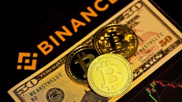 natpis binance ispod njega novcanica dolara i kovanica bitcoina